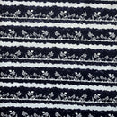 repeating fabric pattern featuring white silhouettes of tropical island scenes on a dark navy blue background. The scenes include palm trees, small thatched-roof huts (tiki huts), and sailboats, arranged in horizontal bands separated by textured, wave-like white lines.