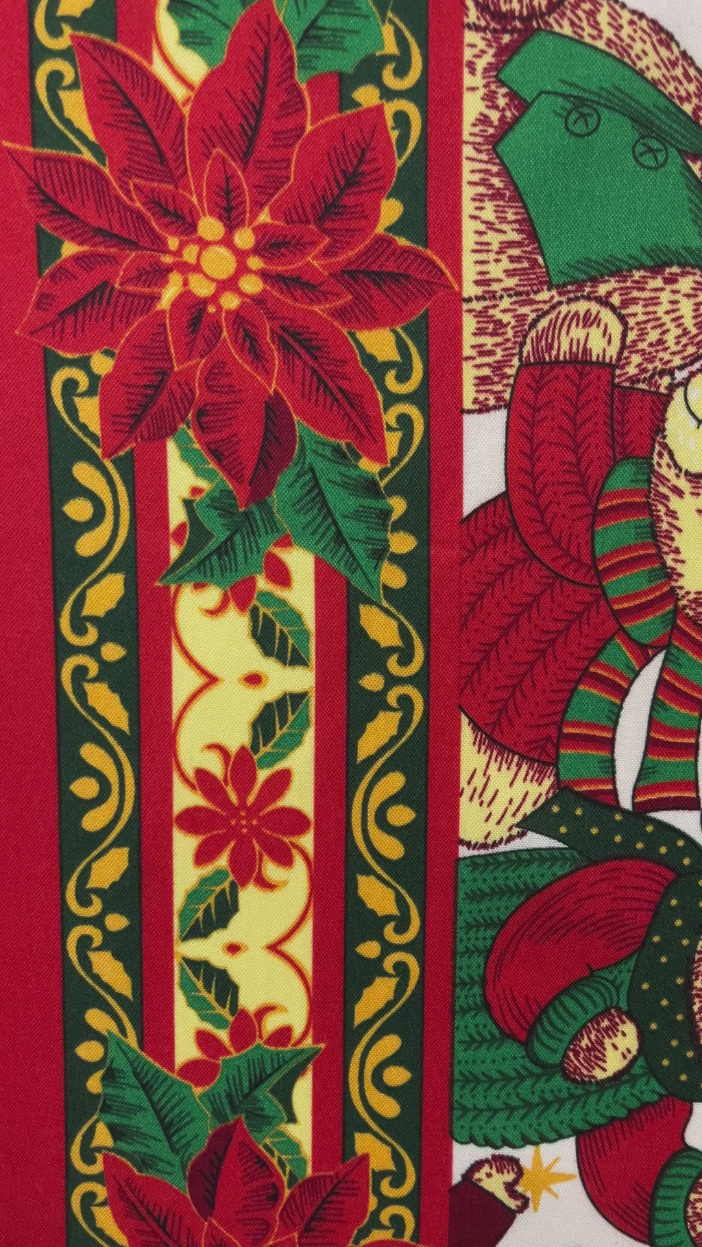 A close-up view of a festive Christmas fabric featuring vertical decorative bands. One band shows a large red poinsettia with green leaves, while an adjacent band features a teddy bear wearing a red and green striped winter hat and scarf on a cream-colored background with ornate gold patterns.